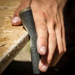 Hand met schuurpapier die de tafel schuurt