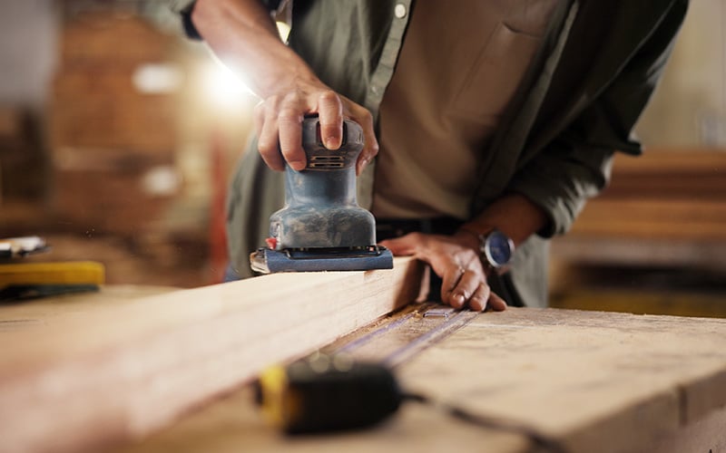 Vakman schuurt een houten plank met een schuurmachine in de werkplaats.